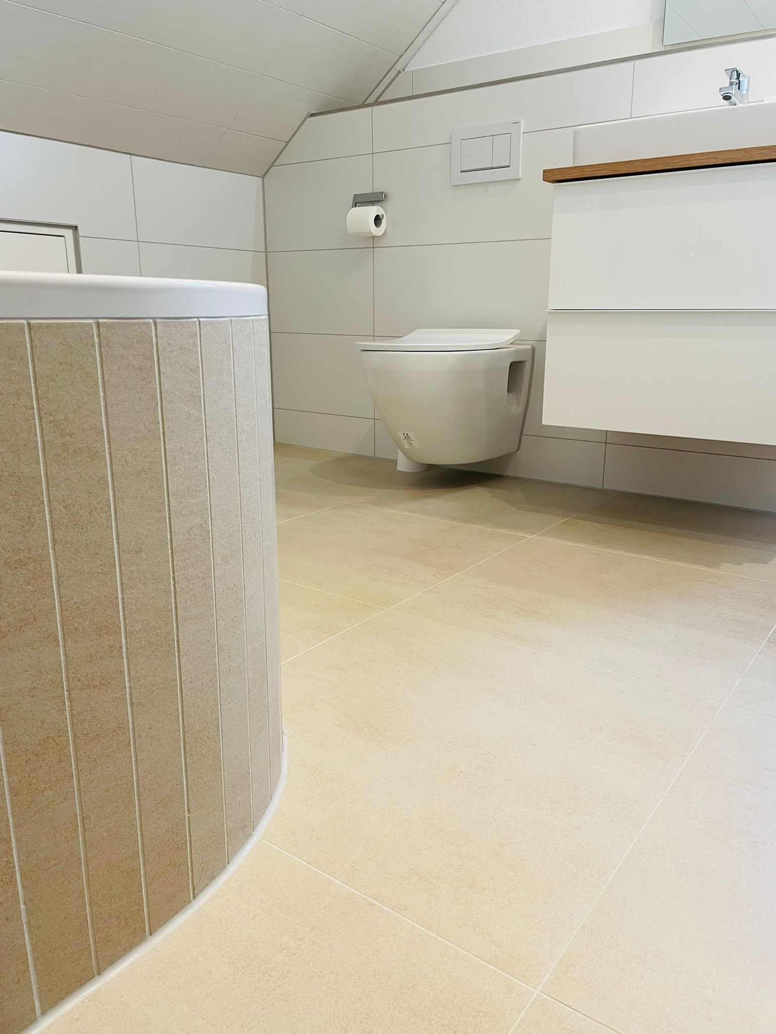 Bad mit hellen Wandfliesen und einer gerundeten, in Travertinoptik verkleideten Wanne