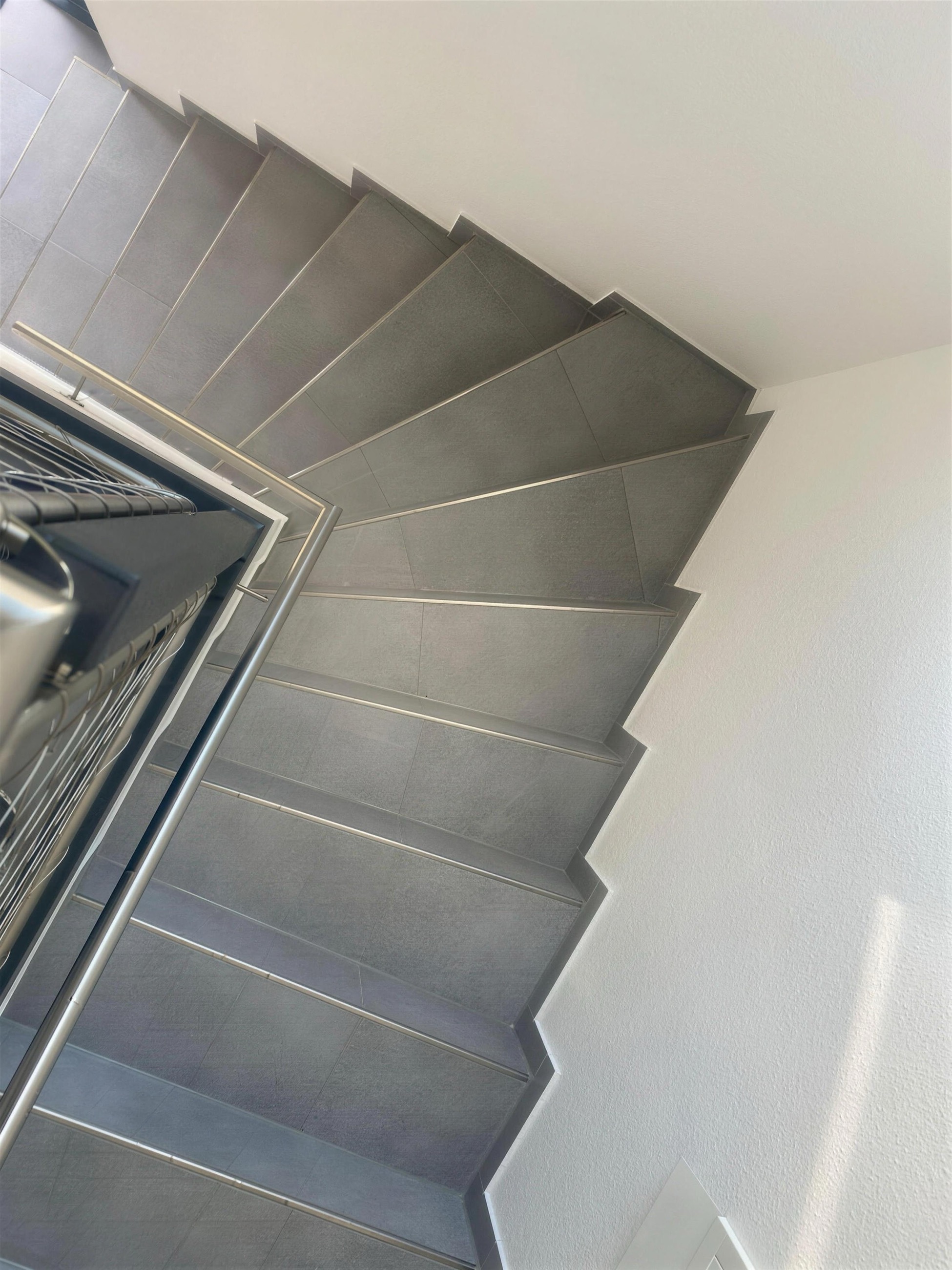Gewendelte Treppe mit Feinsteinzeugstufen in Betonoptik und Edelstahl-Kantenprofil